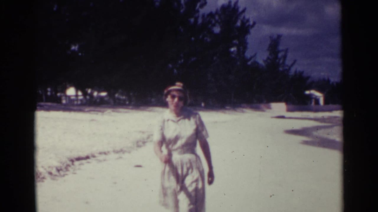 Woman in hat and sunglasses closer to camera on a bright beach.