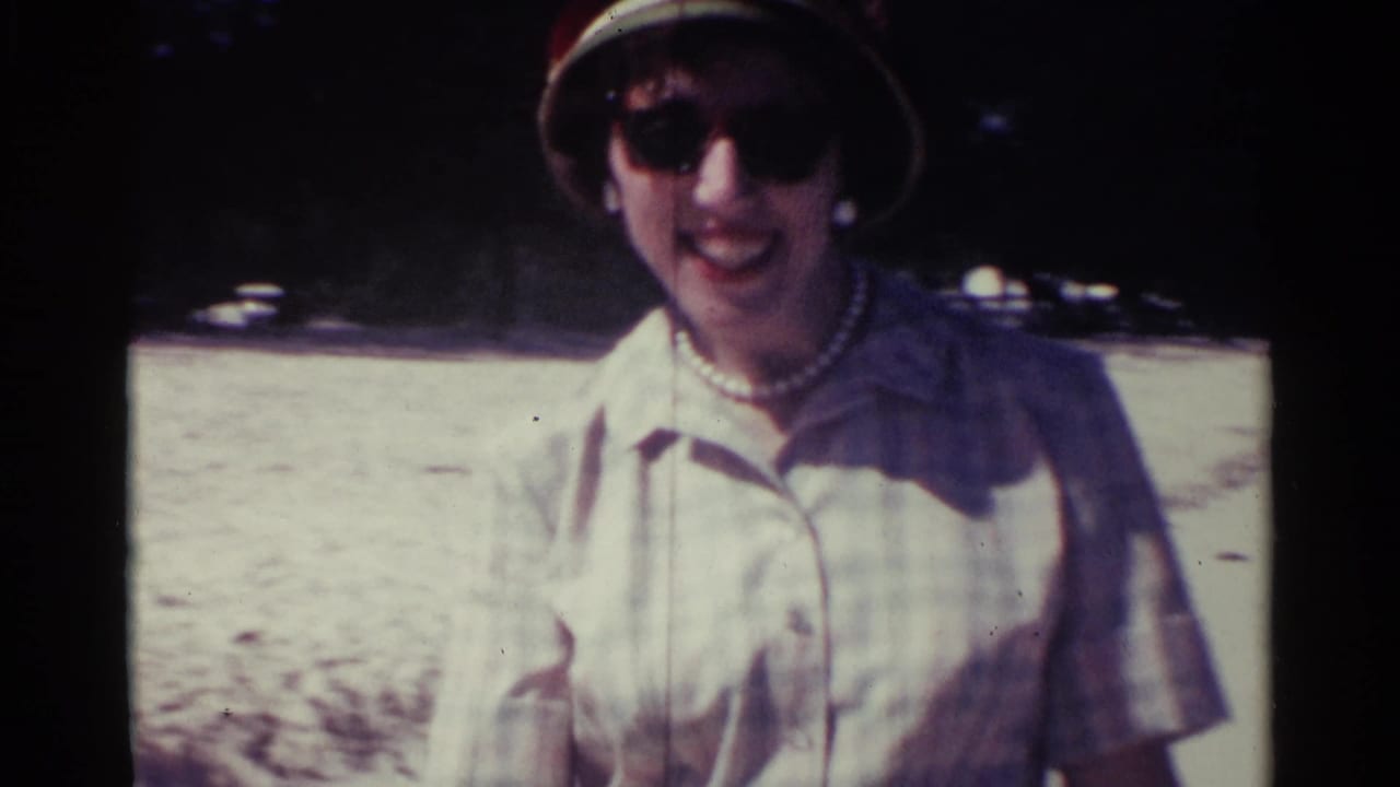 Woman in a brimmed hat and sunglasses smiles outdoors in bright sun.
