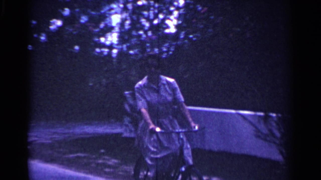 Woman riding a bicycle toward the camera on a shaded sidewalk.