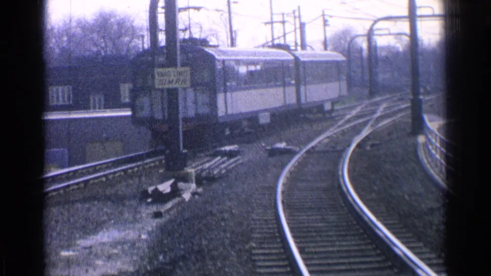 1965 Ohio rail scene with passenger cars rounding curved tracks past station signage, poles, and a low building.