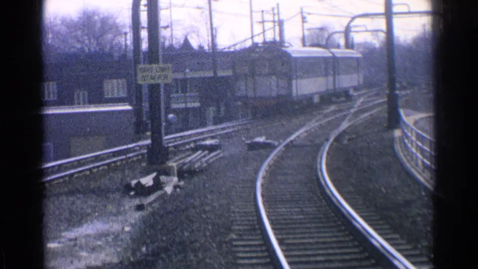 Blue-and-white passenger train recedes on curved Ohio tracks, with overhead wiring and station structures visible in the frame.