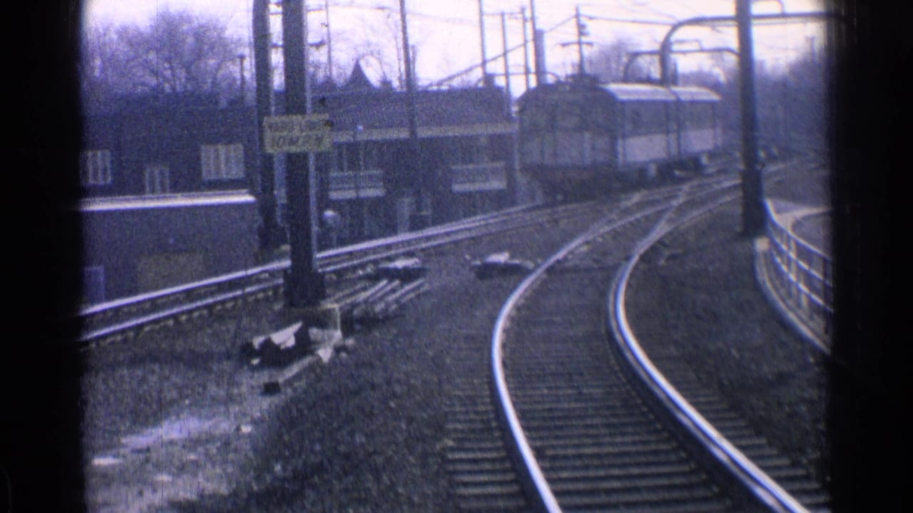 1965 Ohio 8mm frame showing curved rail tracks, overhead wire supports, and a posted rail speed sign near an elevated station area.