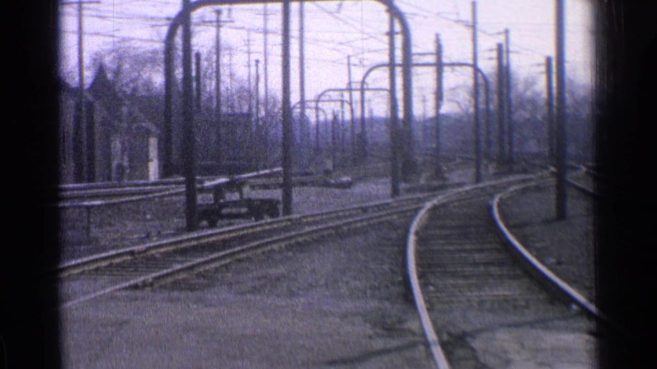 Curved rail tracks with overhead power-line supports in a sparse yard.