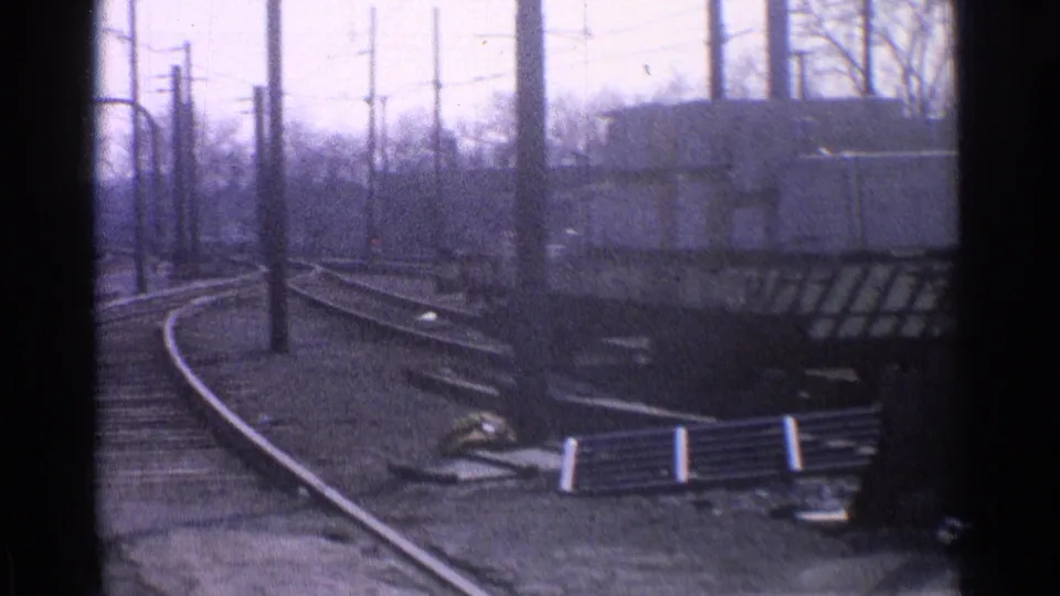 1965 Ohio frame with a trolley or interurban car near a small building, curved tracks, overhead poles, and rail-yard ground details.