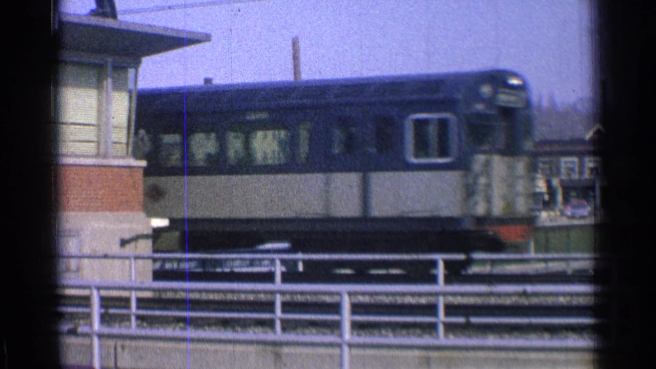 Blue-and-cream train passing elevated tracks beside a station structure.