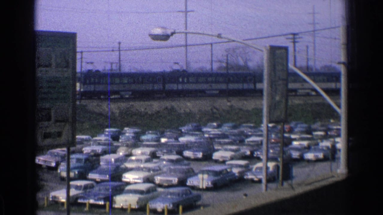 Station parking lot filled with cars while a passenger train moves in the background.