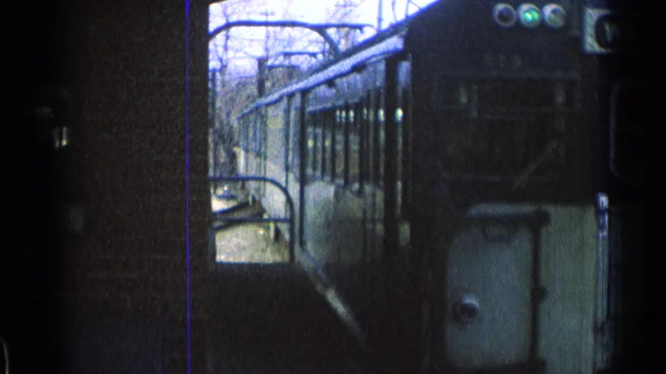 A close 8mm view shows the train passing beside the station platform, with its side windows and front corner visible.