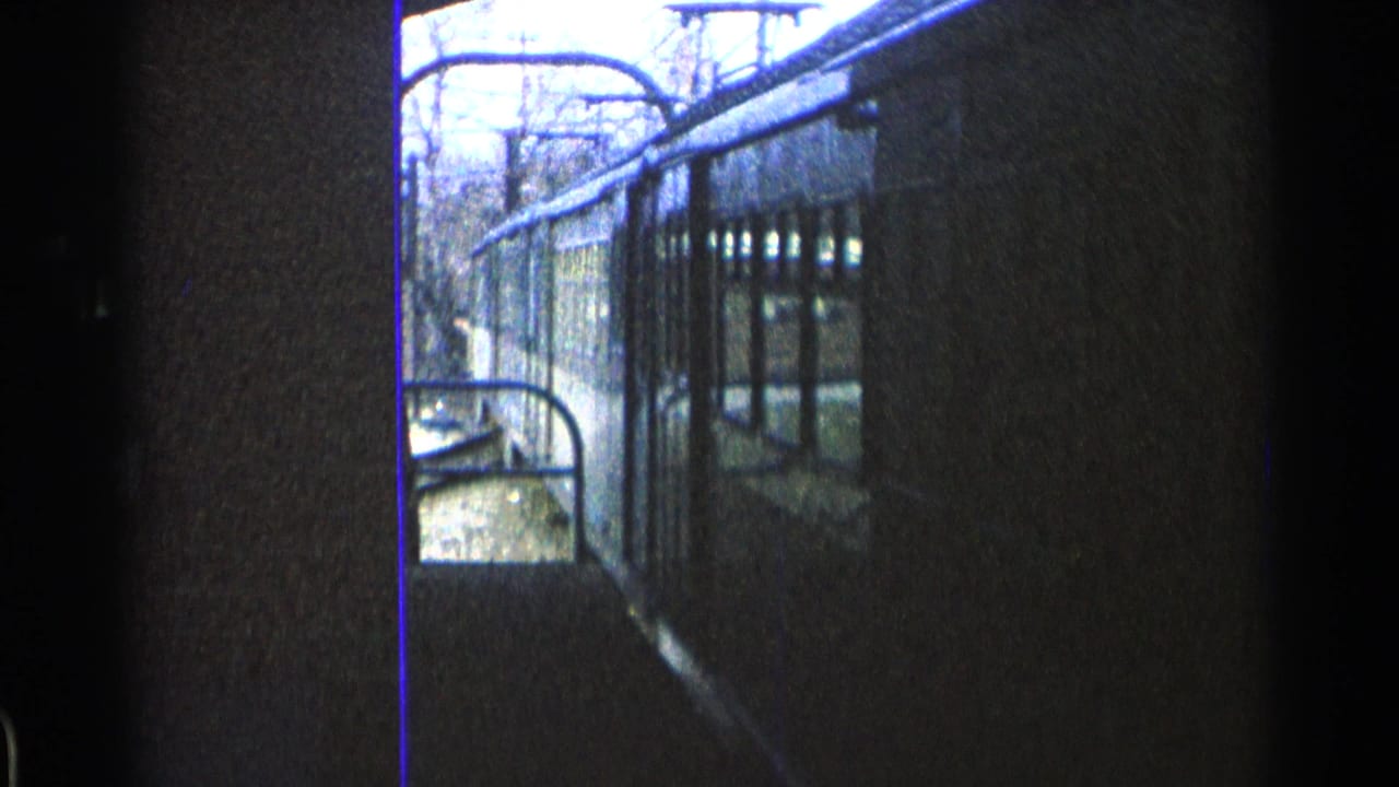 1965 Ohio 8mm frame showing a close side view of a yellow rail car beside tracks, partly obscured by dark framing and film edge.