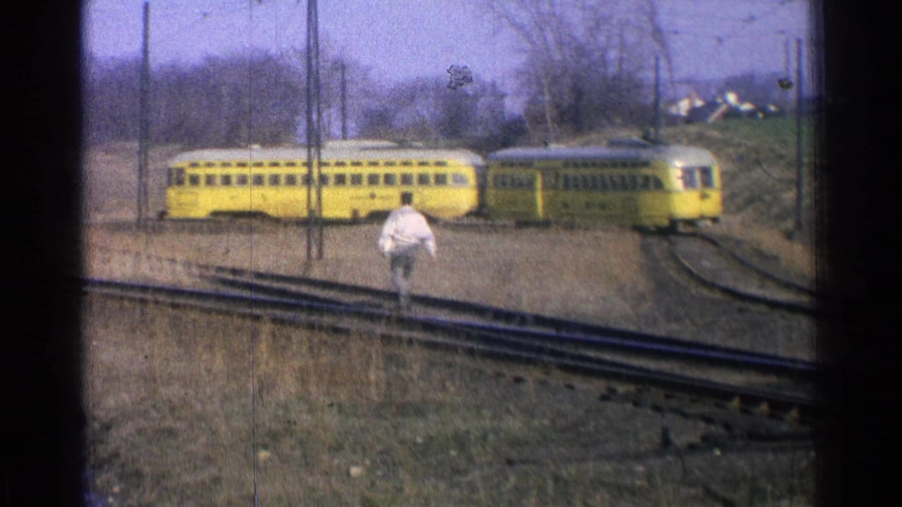 Yellow train cars on rural tracks with one adult walking across the rails.