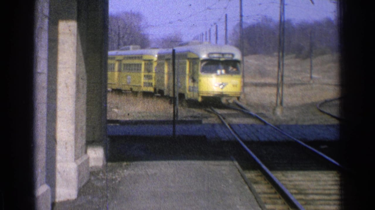 1965 Ohio 8mm frame of a yellow electric train approaching a station platform under overhead wires.