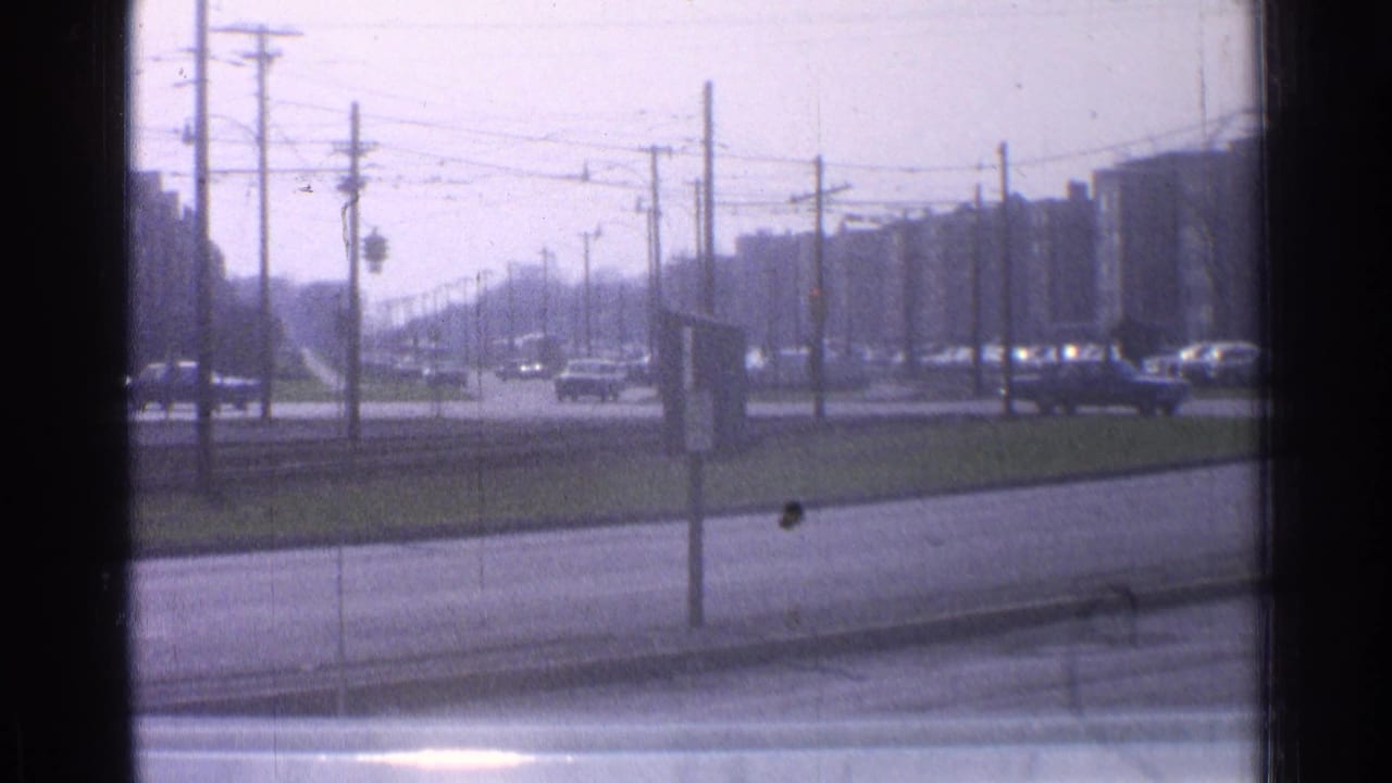 Mid-1960s Ohio roadway scene with sedans and a station wagon passing under dense overhead wires near apartment buildings.