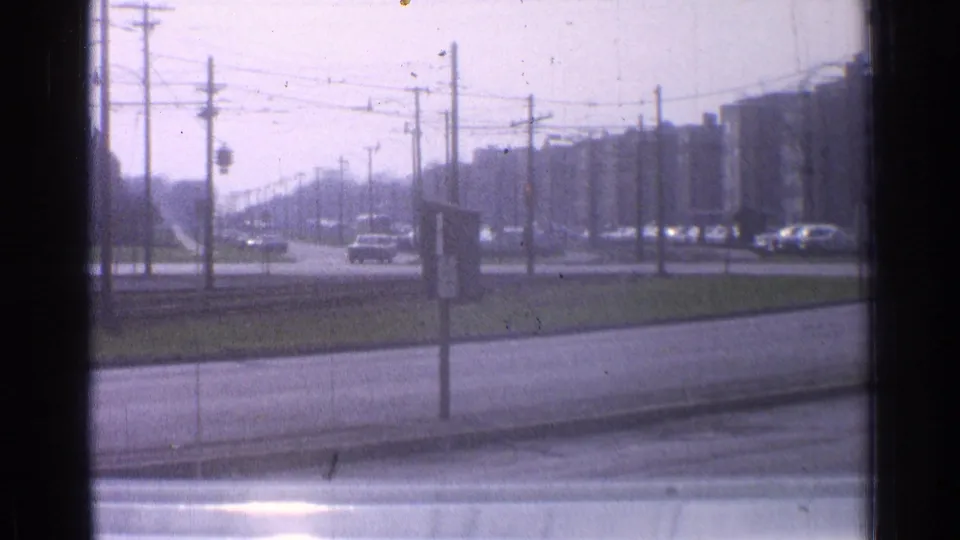 Final frame of a 1965 Ohio street view, with sparse traffic under overhead wires and tall apartment blocks in the background.