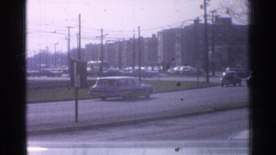 1965 Ohio downtown street with a station wagon crossing the frame, other cars nearby, and overhead wires above the roadway.