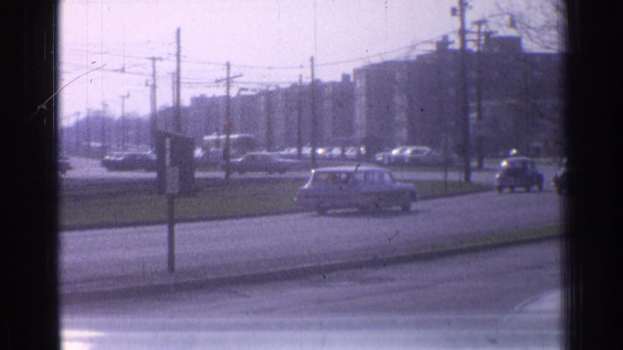 1965 Ohio urban traffic seen through a window, with cars, utility poles, overhead wires, and block-like buildings in the distance.