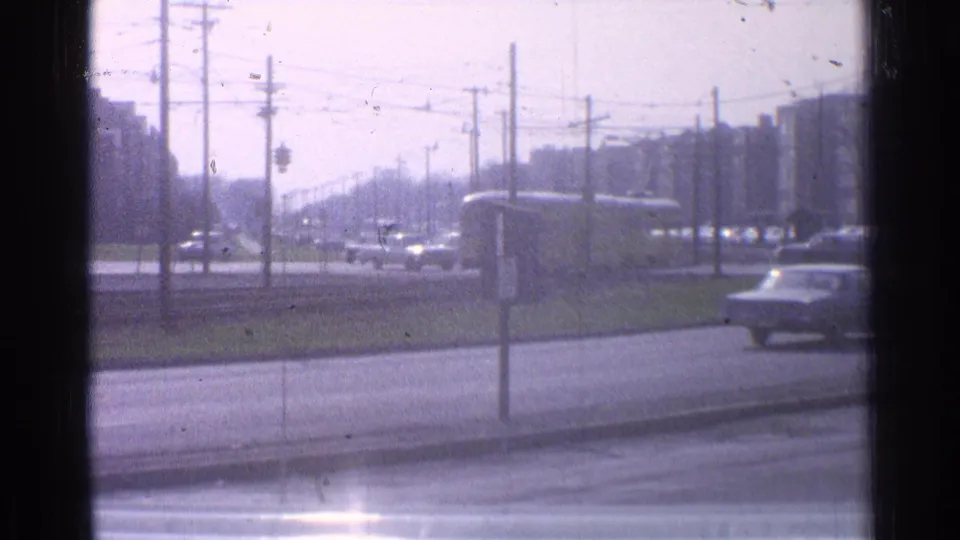 1965 Ohio urban roadway scene with cars, a grassy median, utility poles, overhead wires, and distant block-like buildings.