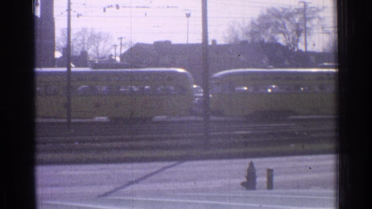 Yellow passenger train behind tracks and wires, seen through a dark window frame.
