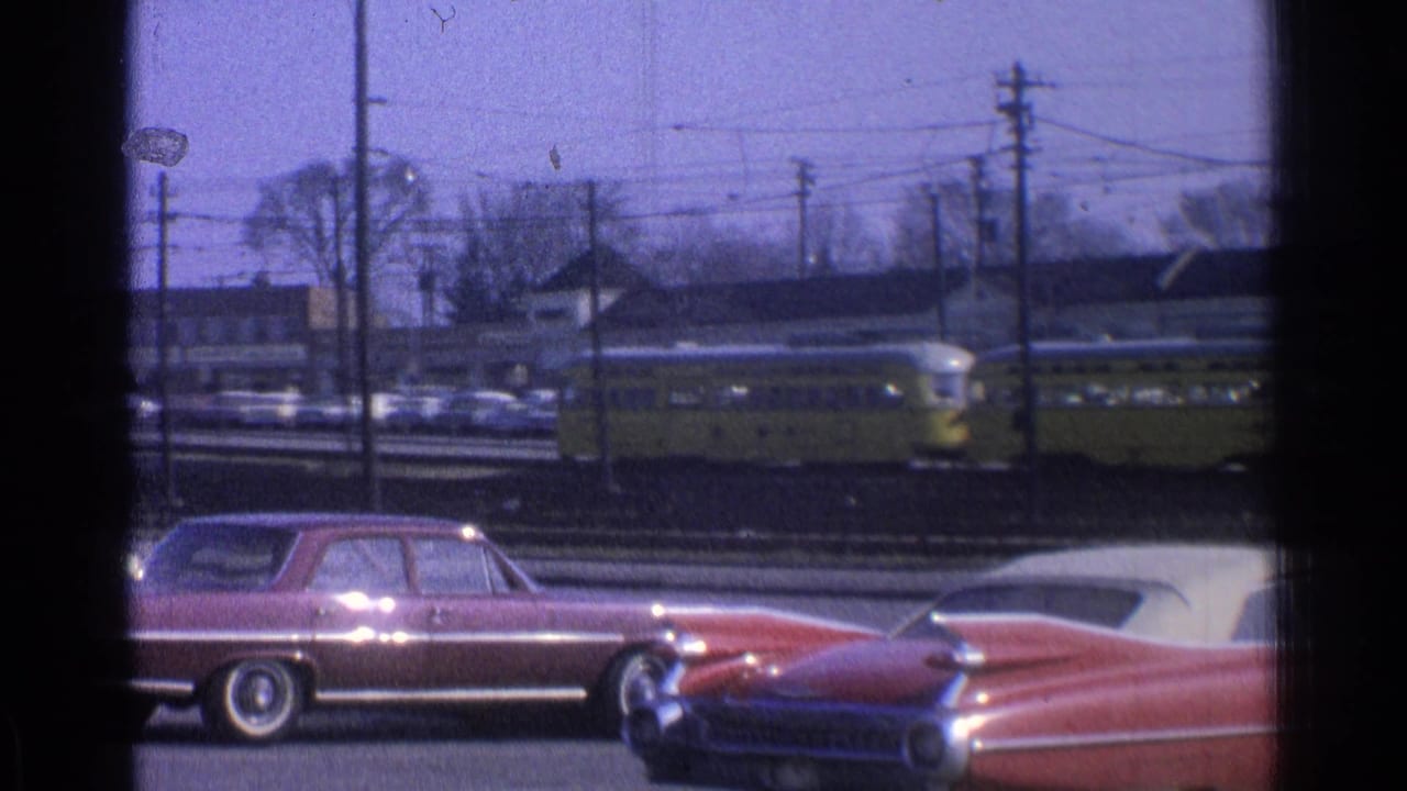 Yellow trolley behind a maroon sedan and red convertible on a street with utility poles.