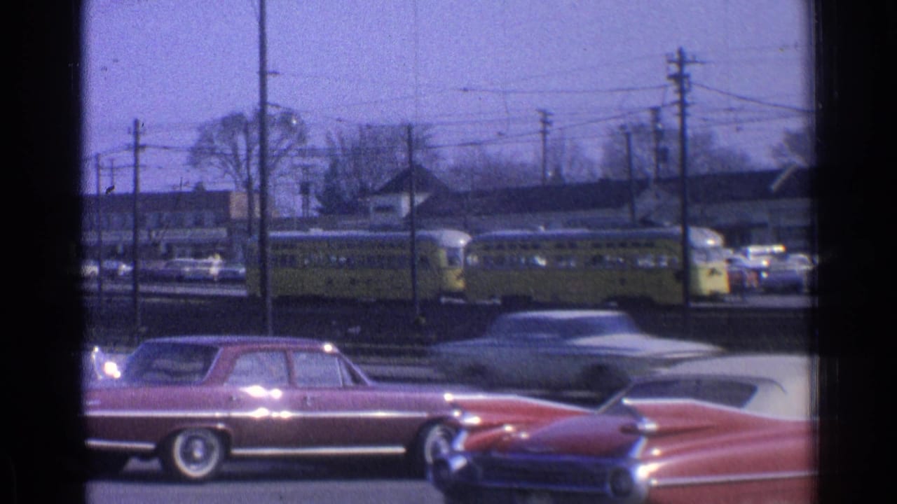 Yellow trolley and classic cars seen across a road with tracks and utility poles.