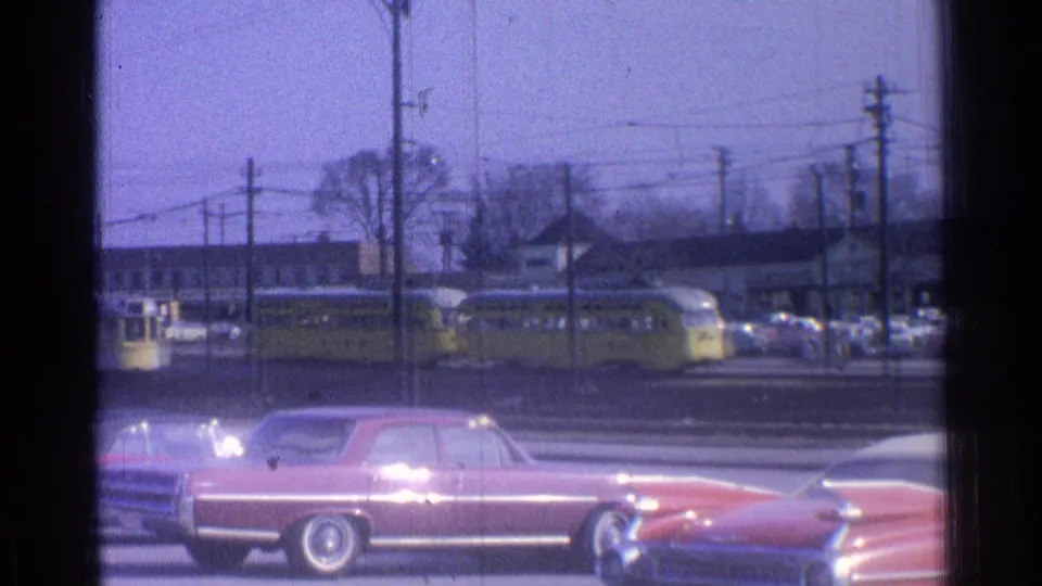 1965 Ohio frame with yellow trolleys in the midground, classic cars along the road, and utility poles crossing the view.
