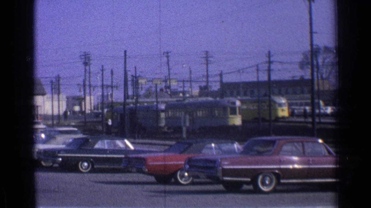 Yellow streetcars pass behind parked classic cars near overhead wires.
