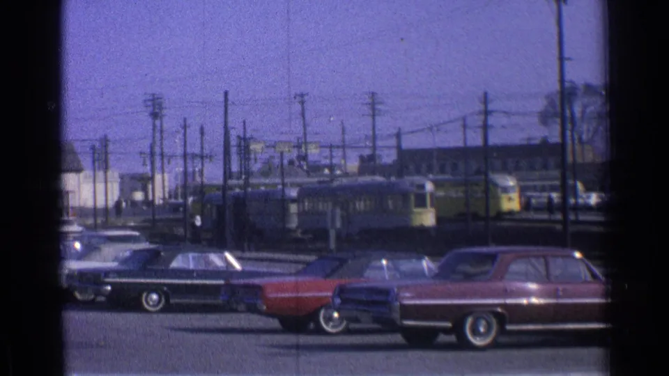 1965 Ohio street scene with yellow streetcars rounding a curve behind parked mid-century cars and utility poles.