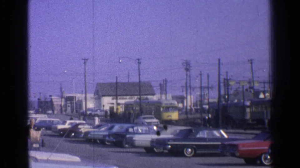 1965 Ohio street scene with classic cars parked along the road while a yellow passenger train moves behind utility poles.