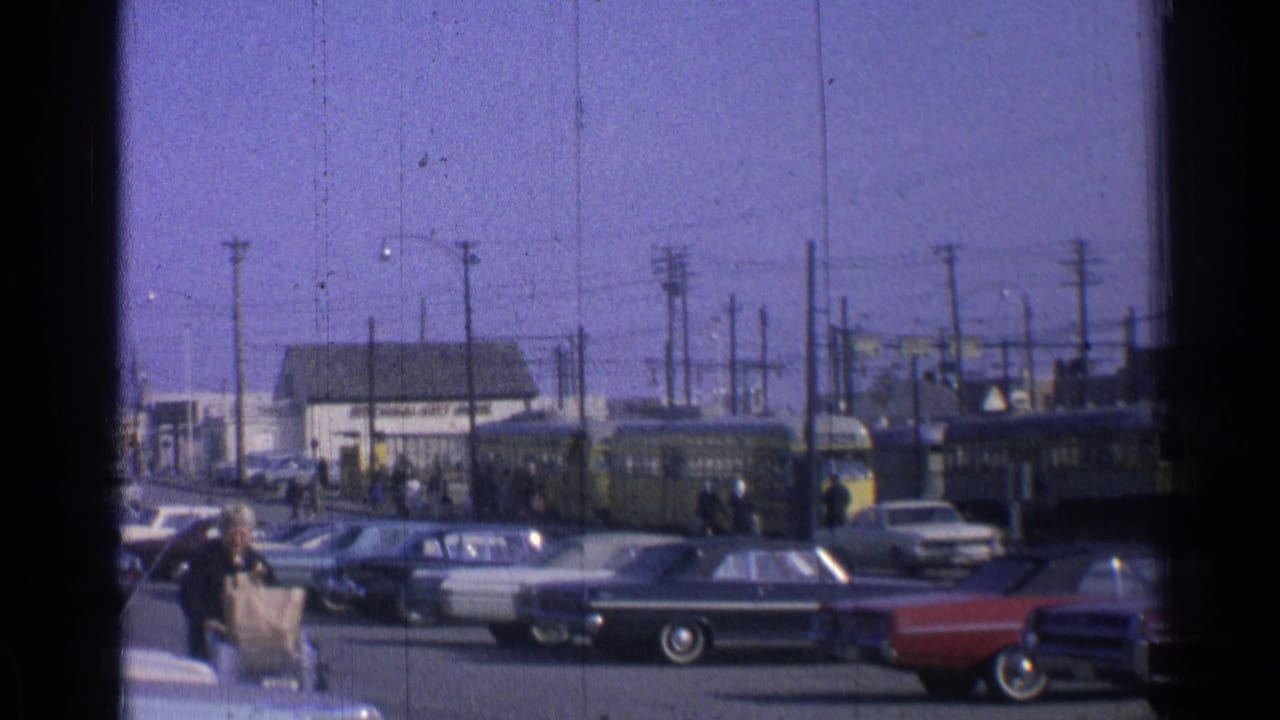 1965 Ohio street scene showing classic cars, pedestrians, utility poles and a yellow trolley or rail vehicle beyond the curb.
