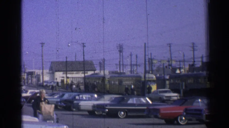 1965 Ohio street scene showing classic cars, pedestrians, utility poles and a yellow trolley or rail vehicle beyond the curb.