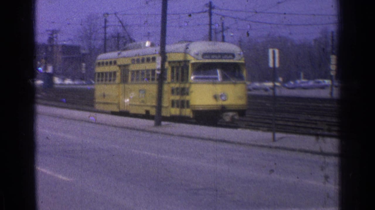 1965 Ohio 8mm frame showing a yellow electric trolley or streetcar on tracks, with overhead wires and roadside poles visible.