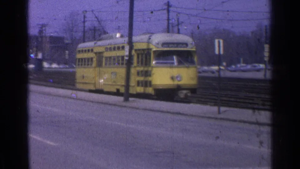 1965 Ohio 8mm frame showing a yellow electric trolley or streetcar on tracks, with overhead wires and roadside poles visible.