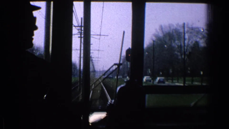 Interior 8mm view from a moving trolley or streetcar in Ohio, with a silhouetted figure and street infrastructure outside.