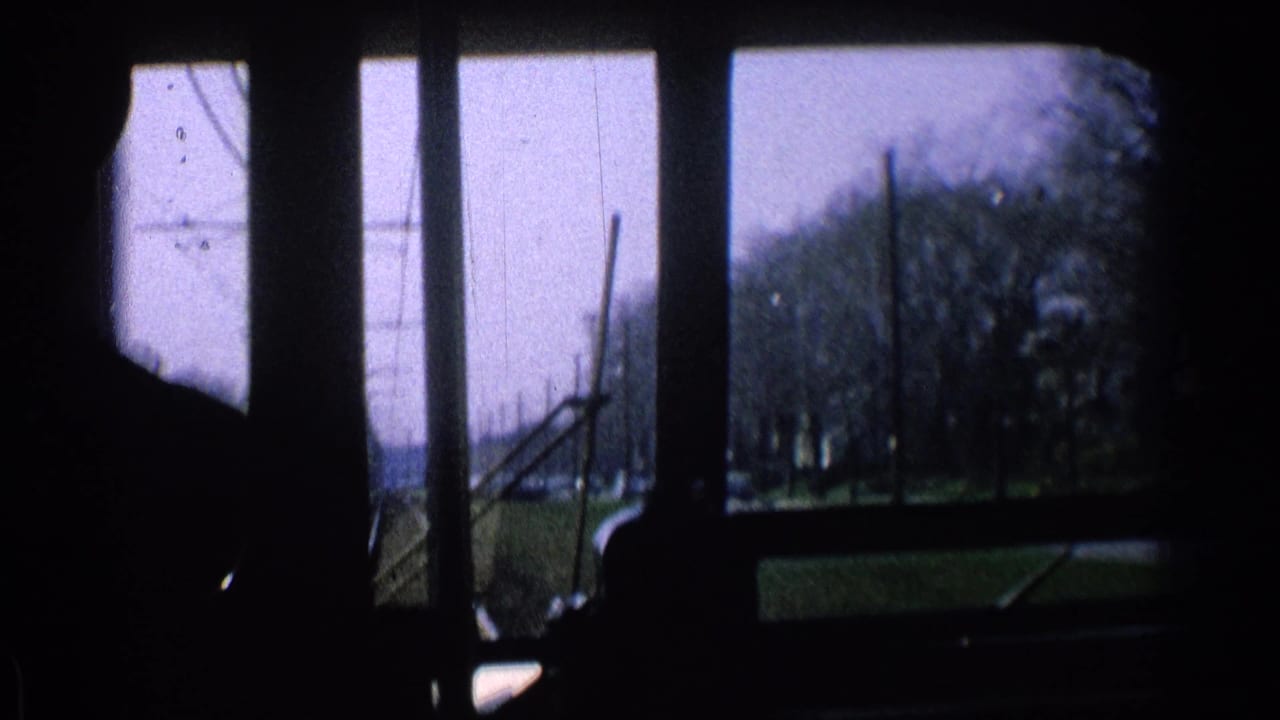 Dark train-cab interior looking through windows toward tracks, poles, trees, and open ground.