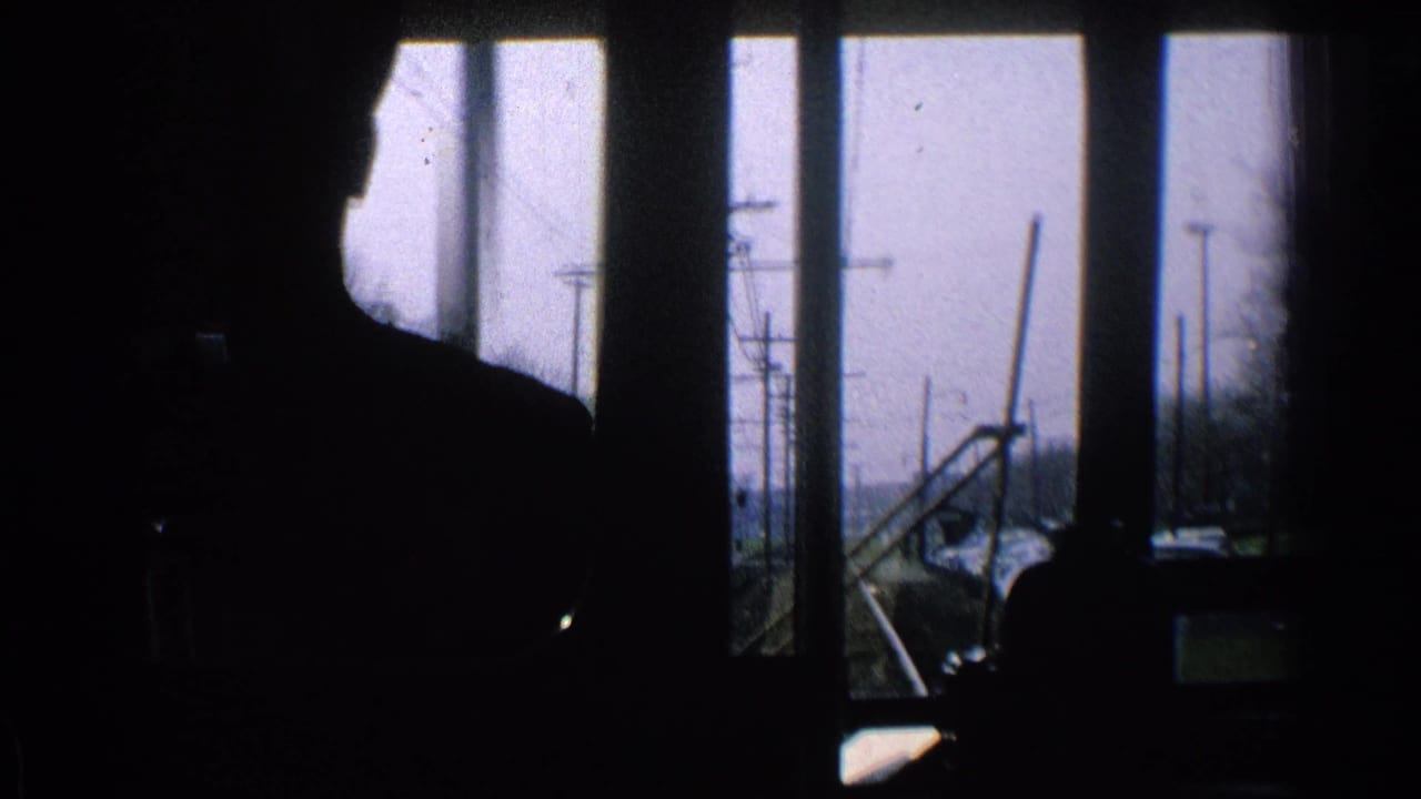 Silhouetted train-cab figure in a 1965 Ohio rail POV, with window frames, tracks, poles, and bare trees outside.
