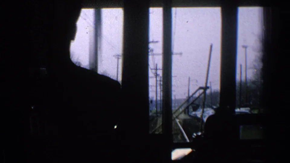 Silhouetted train-cab figure in a 1965 Ohio rail POV, with window frames, tracks, poles, and bare trees outside.