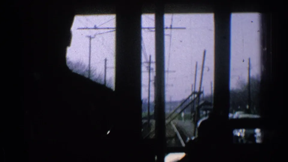 1965 Ohio 8mm interior train view, showing dark cab silhouettes against tracks, utility poles, bare trees, and open land.