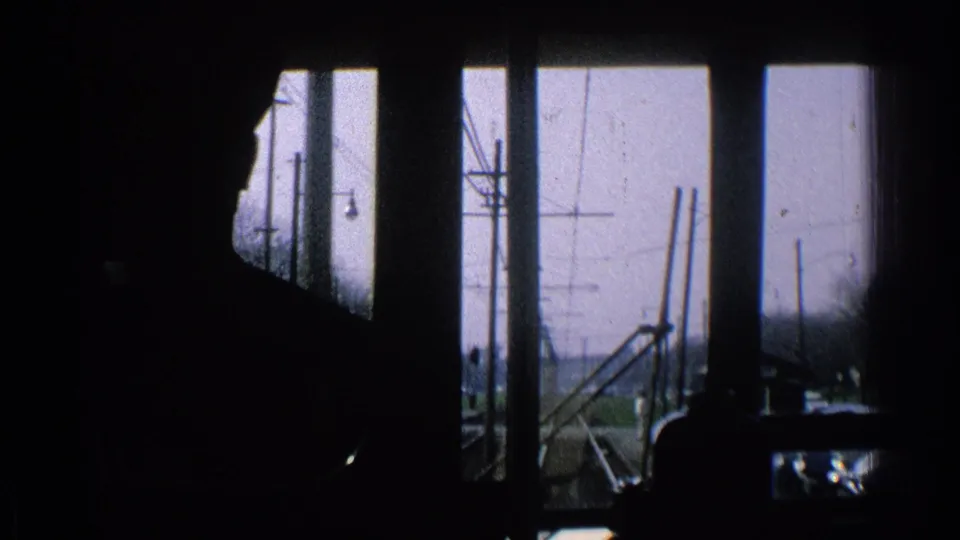 End frame of a 1965 Ohio train-cab POV, with a central silhouette and rural rail infrastructure beyond the windows.