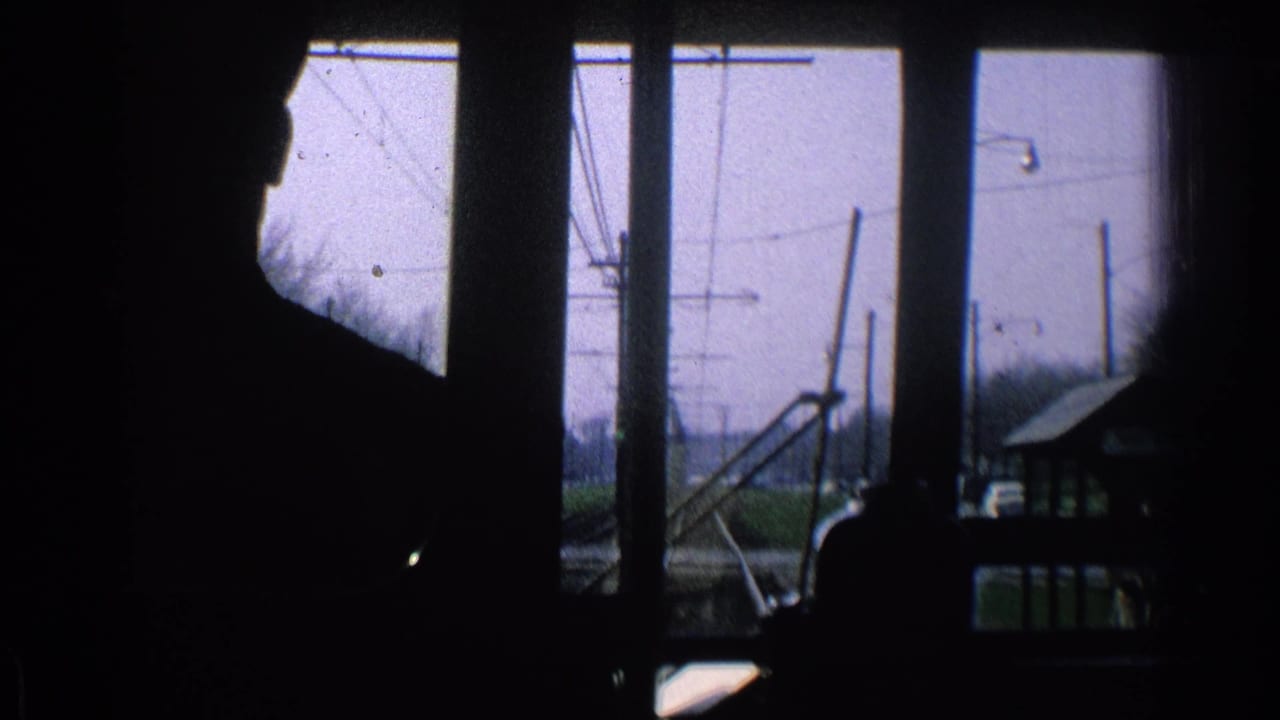 Silhouetted person inside a vehicle looking toward tracks and overhead wires.