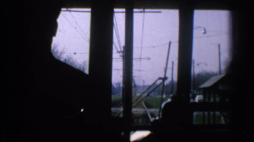 1965 Ohio 8mm frame with a dark passenger silhouette, window posts, tracks, and overhead electric lines beyond the glass.
