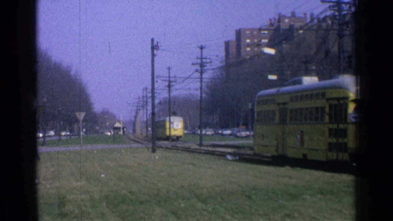 Yellow trolley partly at right with tracks, grass, poles, and a second trolley in the distance.
