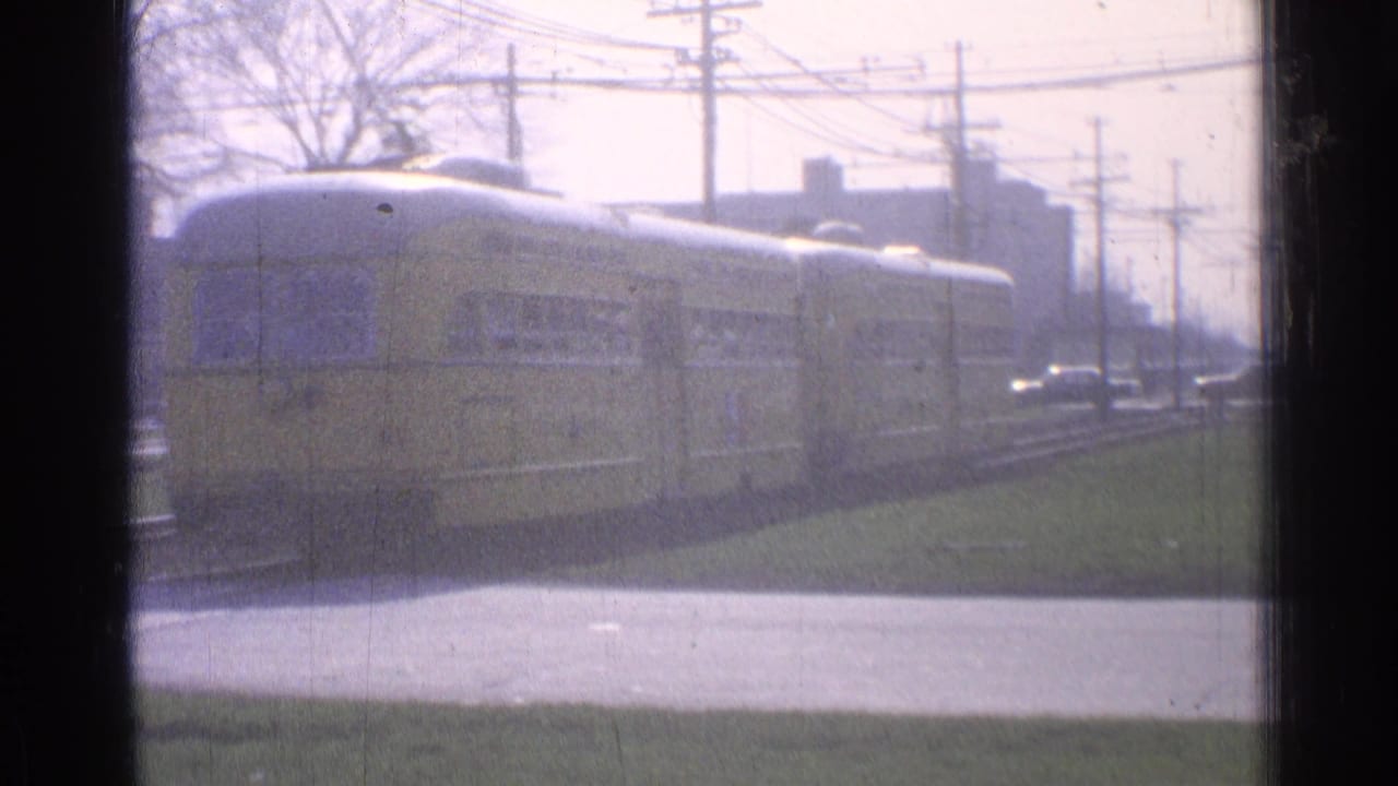Yellow trolley car passing along tracks behind a dark window frame.
