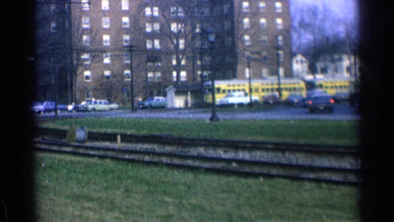 Yellow trolley seen beyond curved tracks and grass with brick apartment buildings behind it.