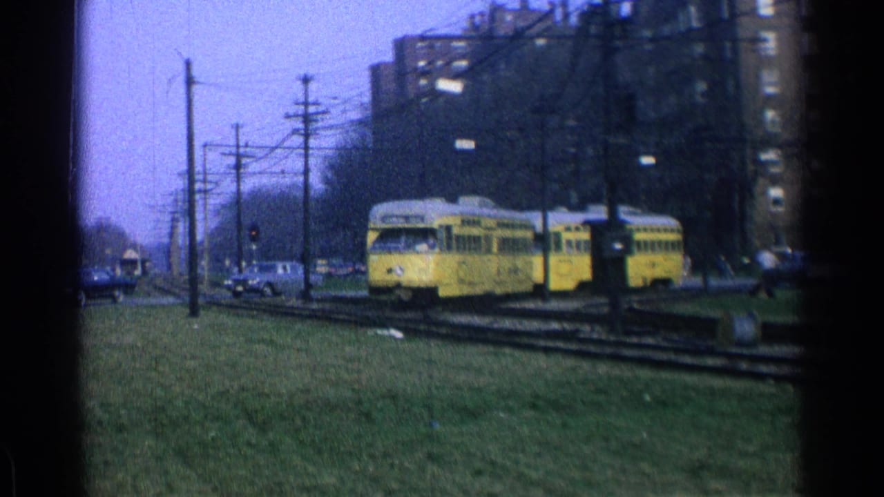 Yellow trolley turning on urban tracks beside grass and apartment buildings.