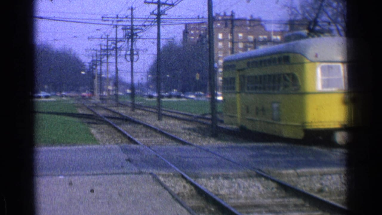 Yellow trolley passing along city tracks with overhead wires and brick buildings in the background.