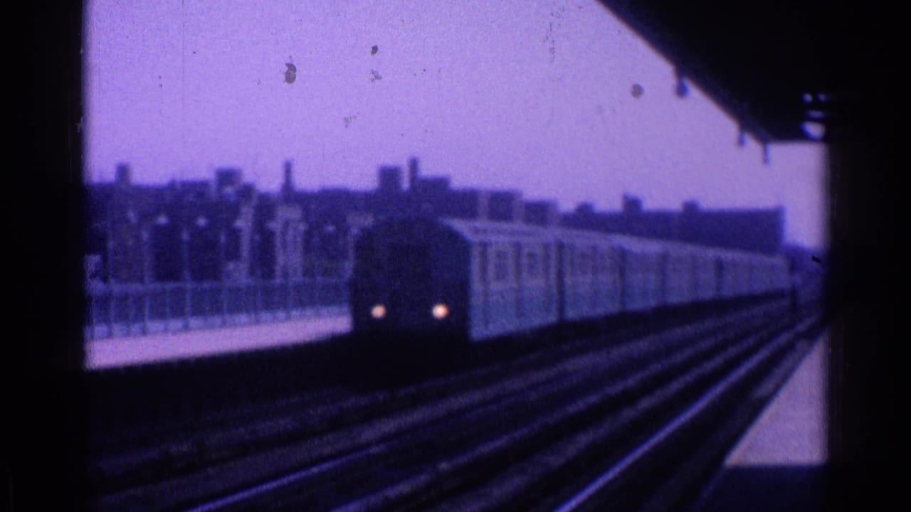 1965 Ohio home-movie frame of a light-colored train approaching an elevated station under a dark canopy edge.