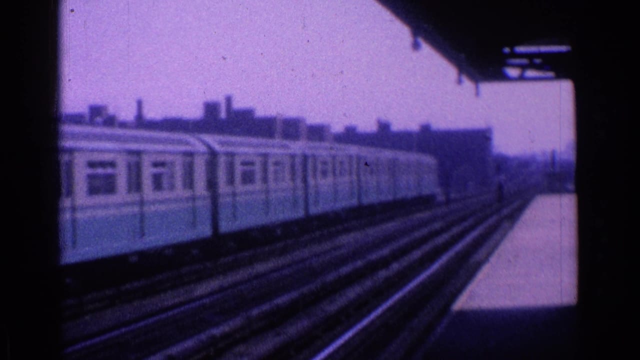 Blue-and-cream passenger train beside elevated tracks under a dark platform canopy.