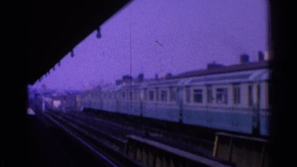 A blue-and-cream passenger train appears to pass an elevated city station in Ohio, filmed from a platform in 1965.