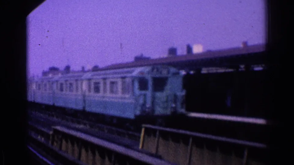 The rear portion of a blue-and-cream passenger train passes a platform canopy on elevated tracks in Ohio, 1965.
