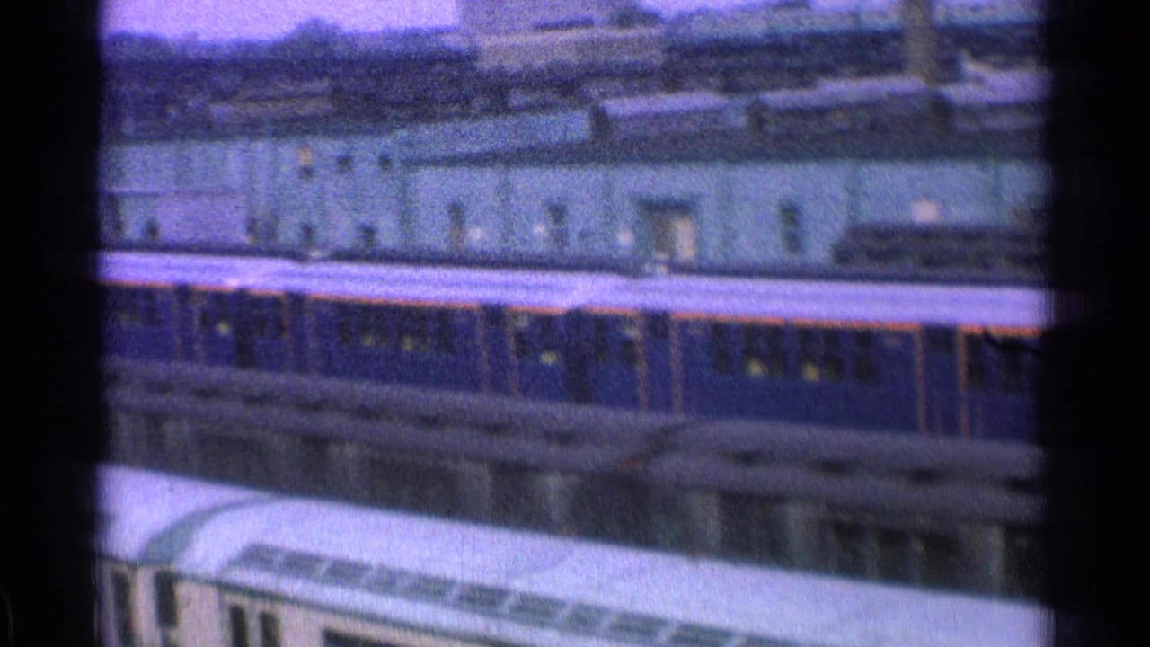 Blue passenger train cars in a rail yard seen from an elevated moving viewpoint.