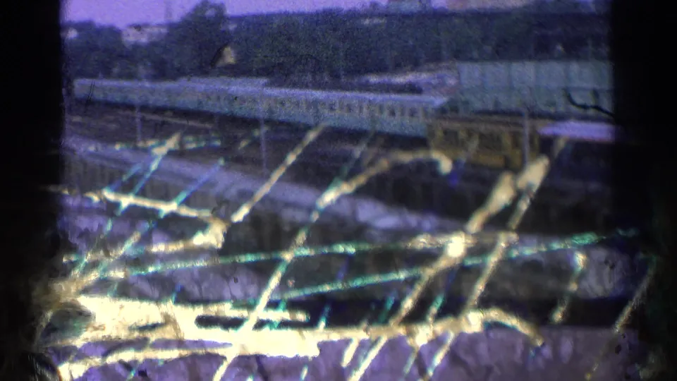 1965 Ohio 8mm frame showing rail cars, tracks, yard structures, and bright scratches or damage across the lower film area.