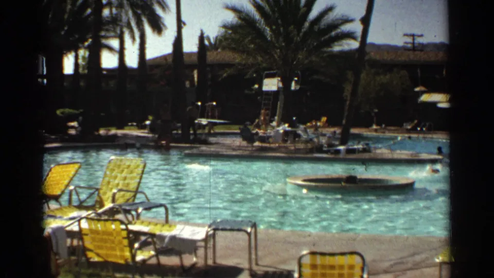 Scottsdale resort pool in 1968 with yellow metal lounge chairs, swimmers, palms, and a circular feature in the water.